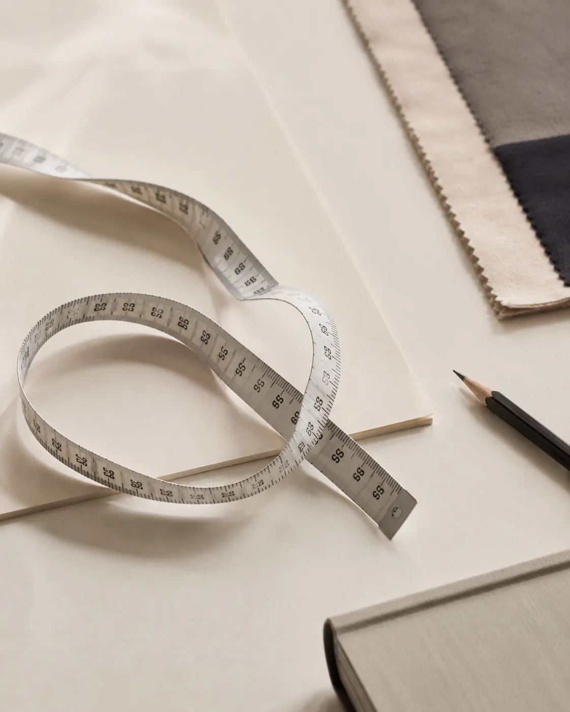Measuring tape, fabric swatches, and a pencil on an ivory desk